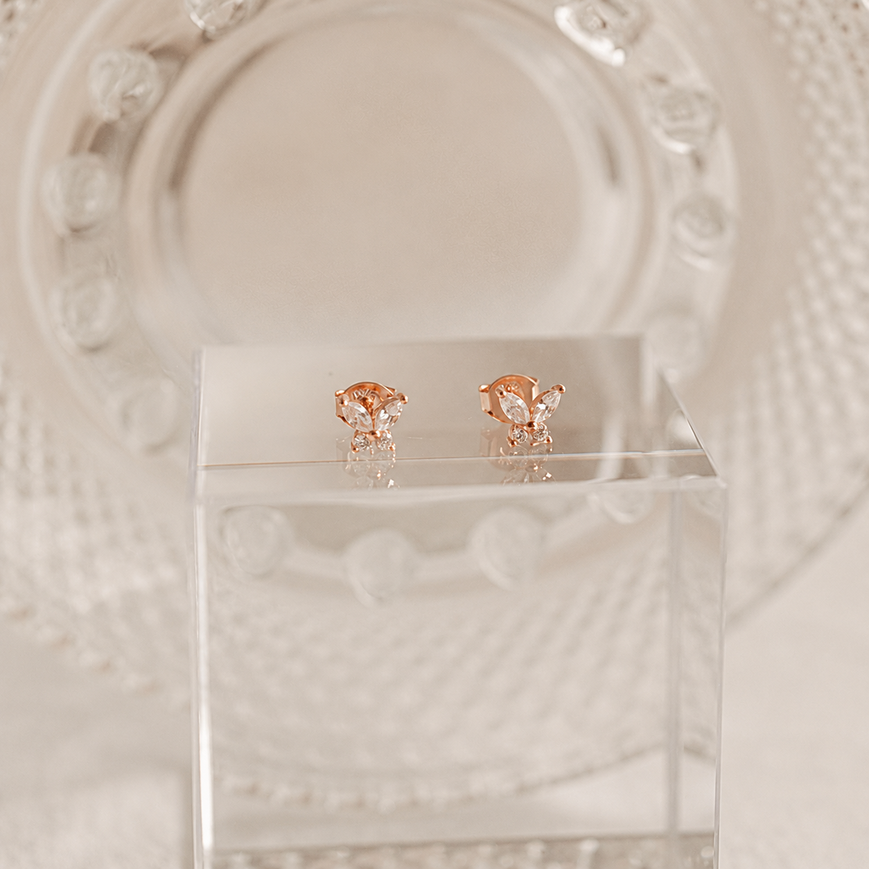 Rose gold butterfly earrings on a clear stand with a decorative white background